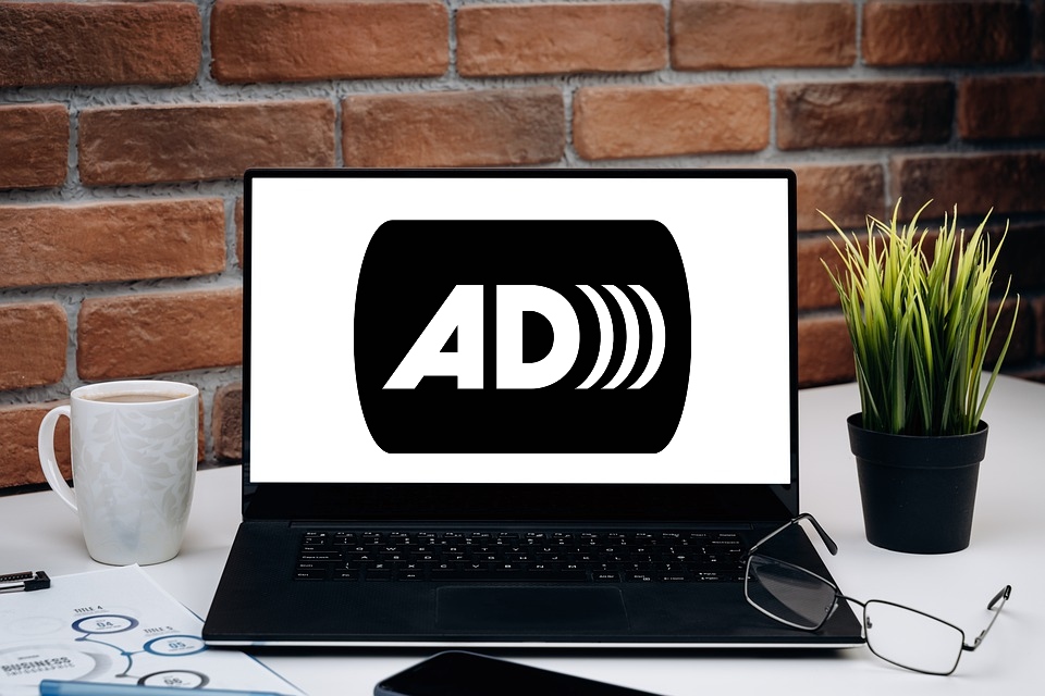 A laptop sits on a desk. On its screen appears the audio description logo. 