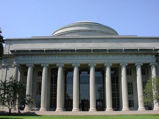 Facade of gray building with a colonnade of 10 round 30 feet tall columns. Along the facade, over the columns, carved is the phrase "Massachusetts Institute of Technology". A dome sits atop the building.