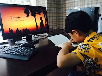 A boy writes on a notebook in front of a screen
