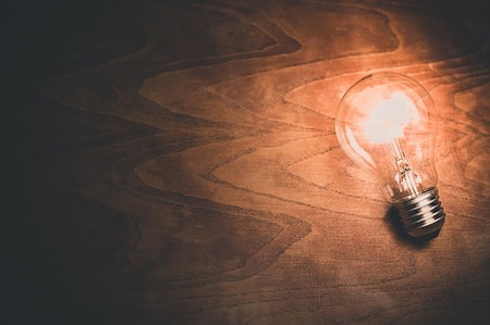A light bulb powered on rests over a wood surface