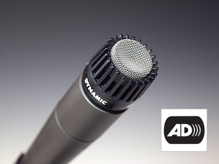 A microphone pointing up and to the right. The letters AD that indicate audio description appear on the the bottom right.