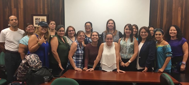 Conference room. A group of teachers poses and smiles before a big projector screen 