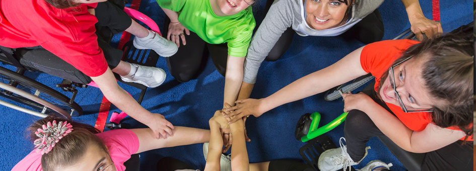 7 women form a circle and each put a hand out to overlap each other at the center and smile looking up