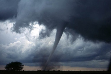 Dark clouds in the sky. From the clouds a tornado swirls down, touches the ground and lifts dust.