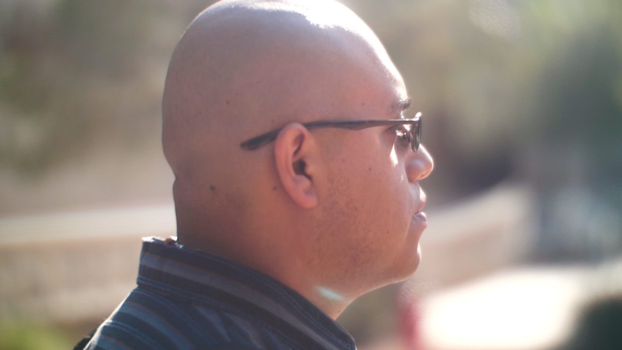 A bald man sitting outdoors.