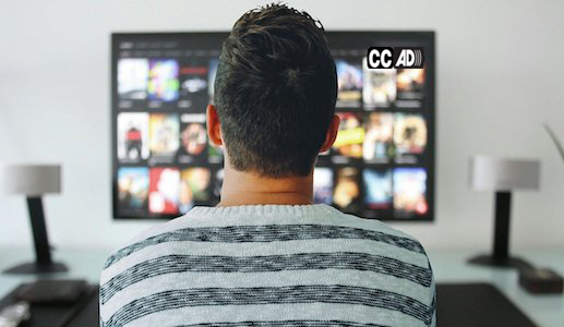 A man seated in front of a TV. On the upper right corner of the TV screen appear the captioning and audio description icons.