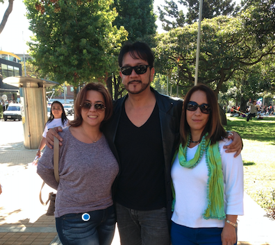 Bogotá. Outdoors, sunny day. Standing, Orlando Arenas embraces Lourdes Fiallos and María Victoria Díaz, at his sides.