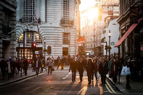 Many people with sweaters and jackets walk on a street