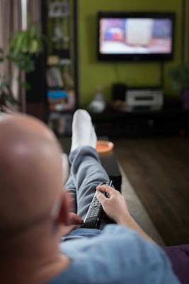A bold person with glasses watches TV